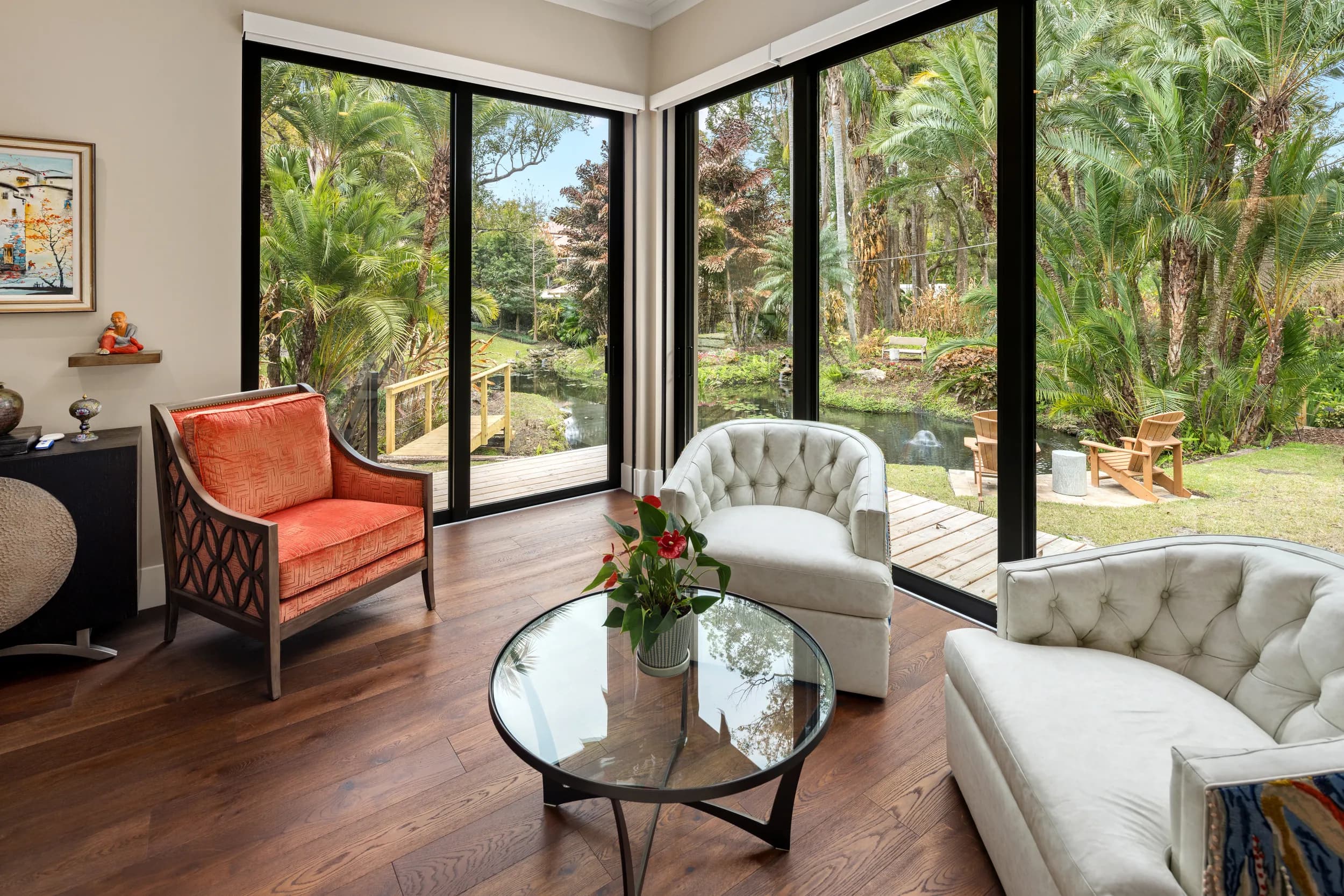 Living room with floor-to-ceiling glass walls opening to a tropical garden and pond