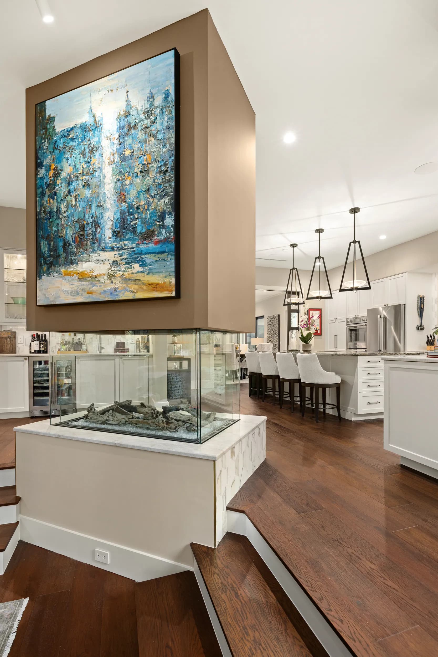 Open kitchen seen past a glass-enclosed double-sided fireplace and abstract art