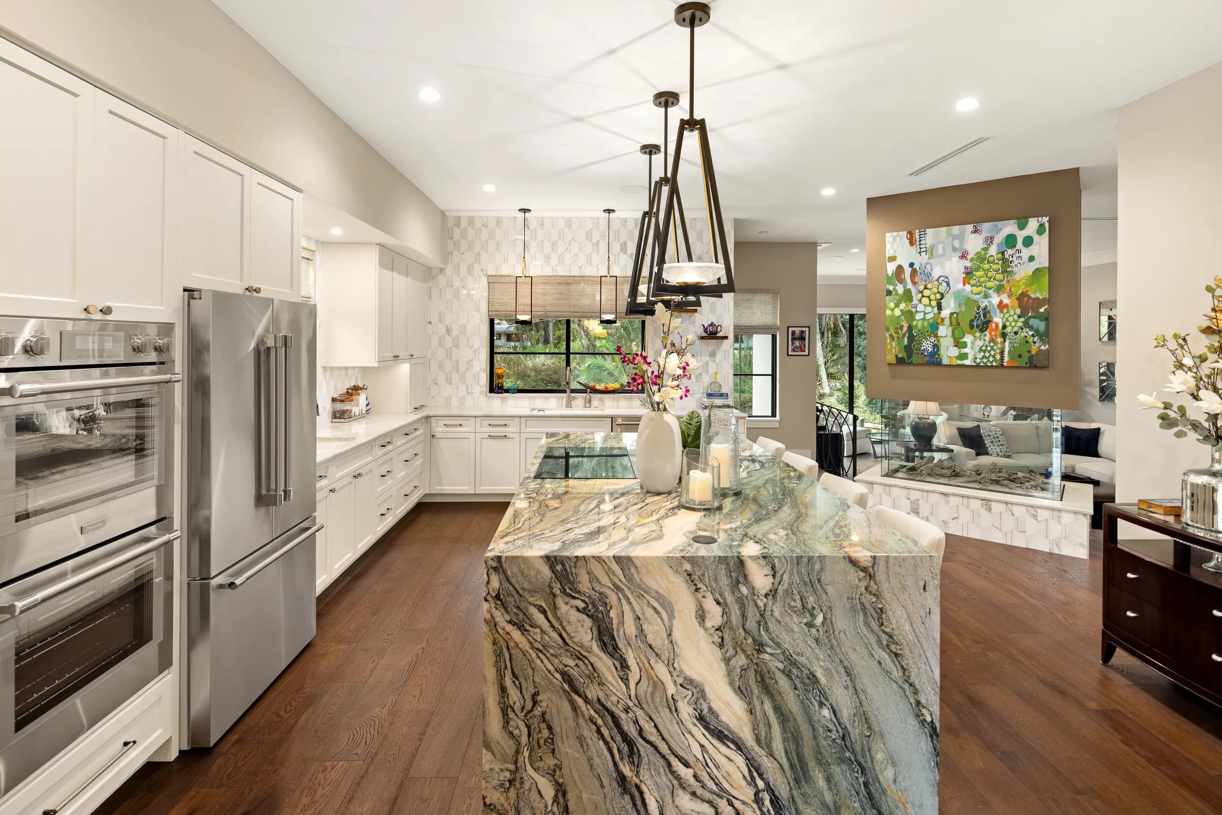 White kitchen with a veined marble waterfall island and black lantern pendants