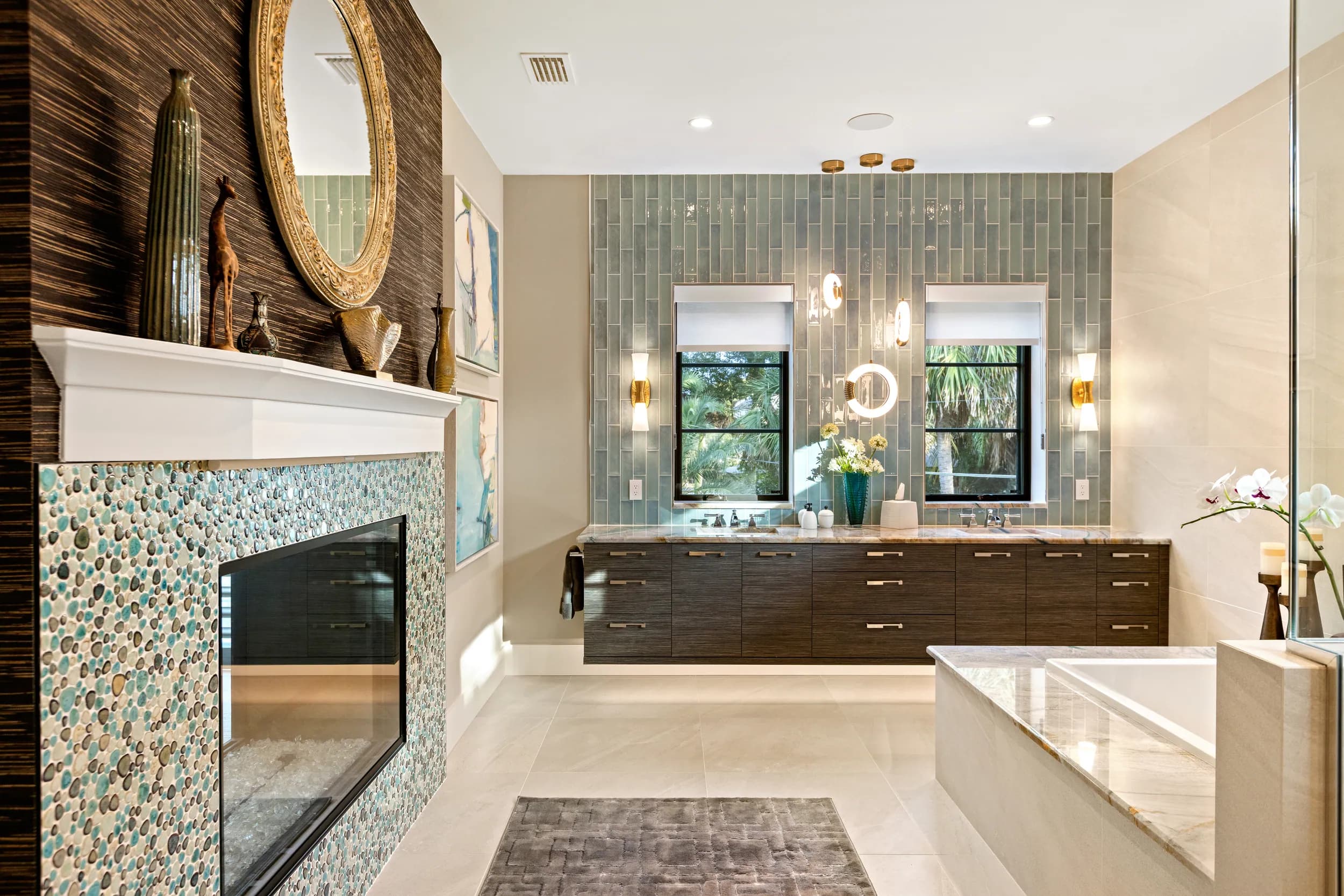 Primary bath with dark double vanity, freestanding tub and a pebble-mosaic fireplace wall