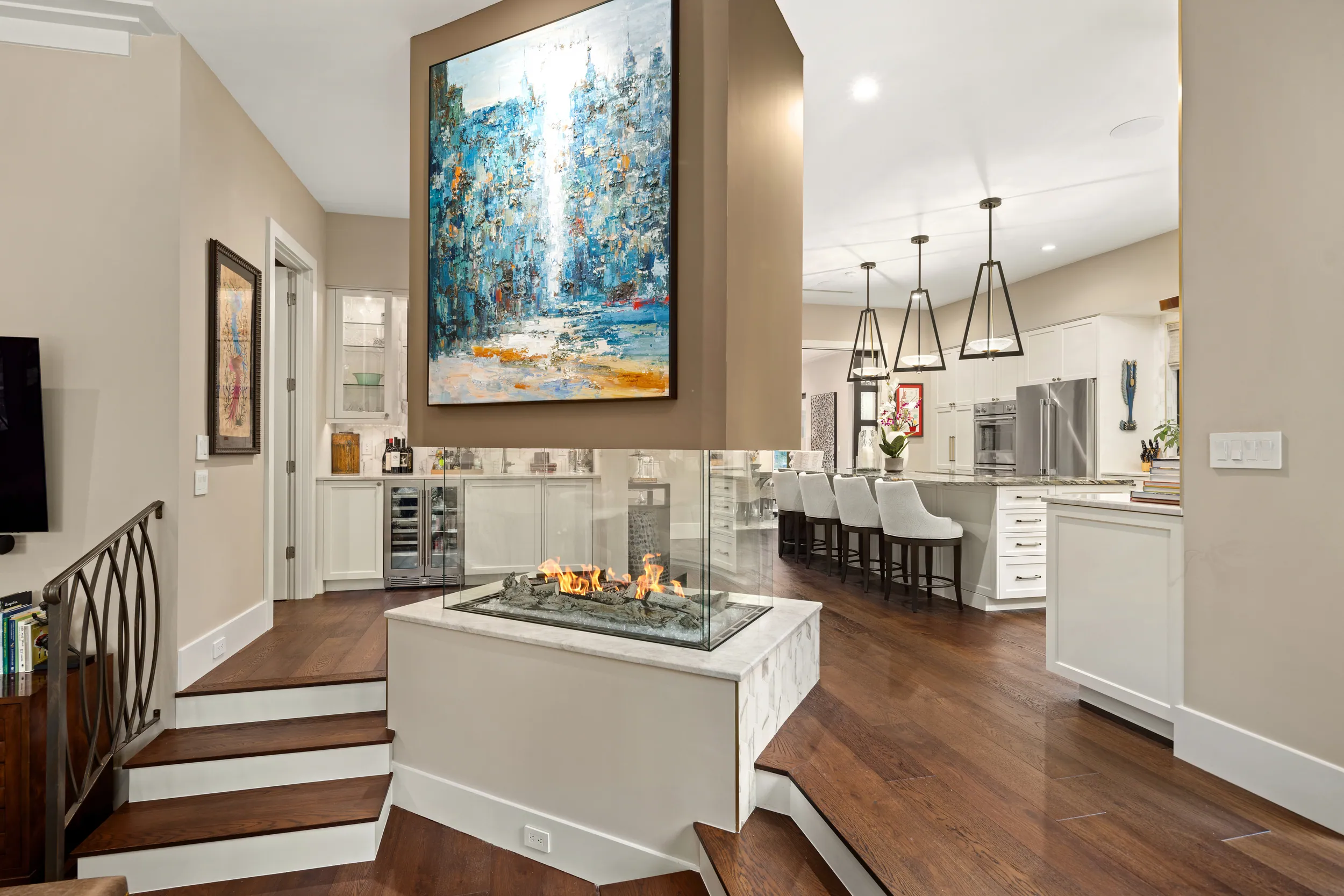 Entry steps down to the kitchen past the glass fireplace and blue abstract art