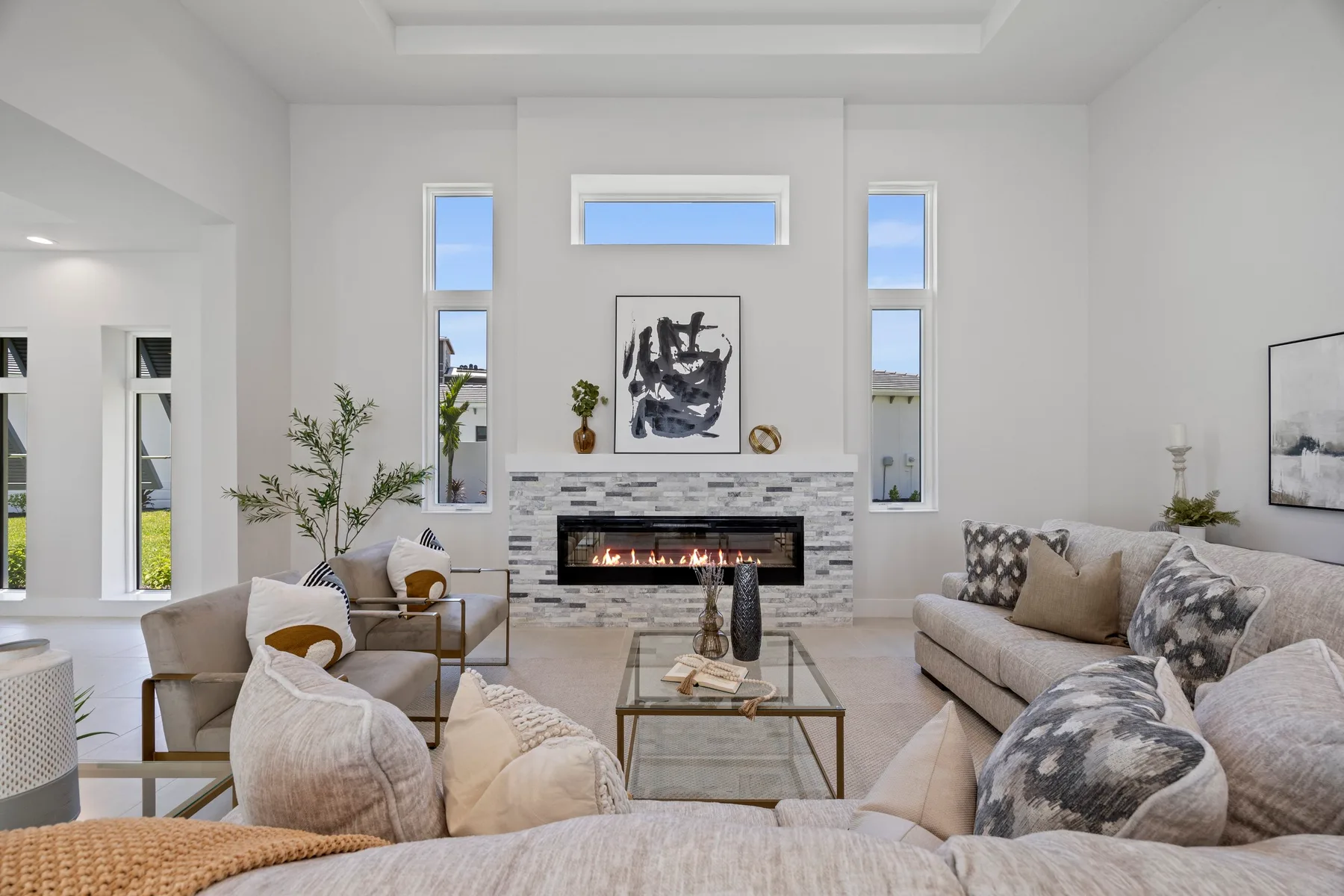 Modern living room with white walls, featuring a fireplace, abstract art, and minimalist furniture. Decor incorporates neutral tones with touches of greenery.